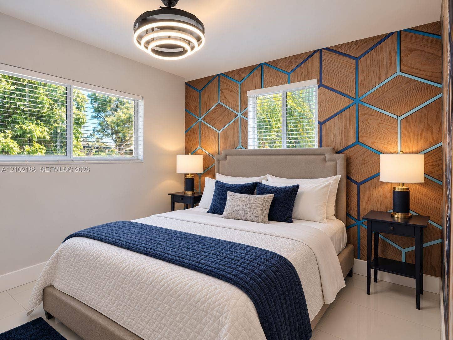 Geometric wood-paneled accent wall with integrated metallic inlay, neutral-toned flooring, large windows with horizontal blinds, and a modern circular LED ceiling fixture