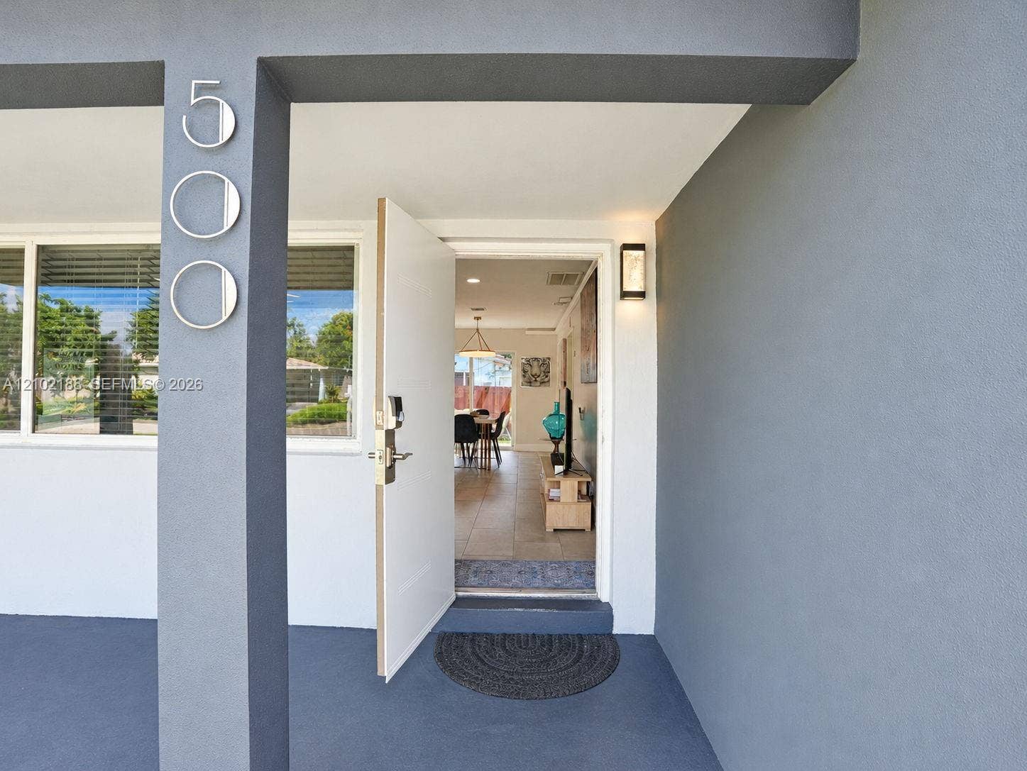 Covered entryway featuring a solid-color stucco exterior, mounted address numerals, and a sleek modern exterior sconce