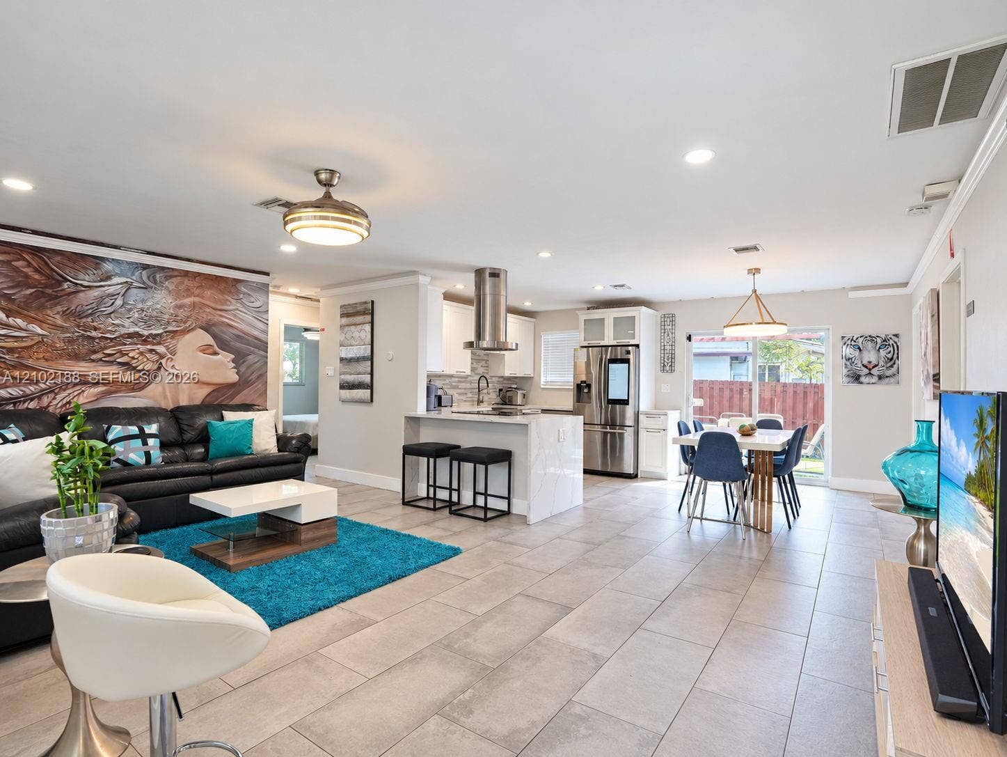 Open-concept area featuring stone-finish flooring, a kitchen island with stone countertop, stainless steel appliances, a cylindrical range hood, and recessed lighting