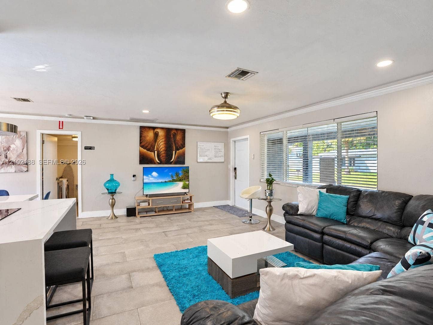 Open-concept interior featuring light-toned tile flooring, recessed ceiling lighting, a contemporary ceiling fan, and large windows with horizontal blinds