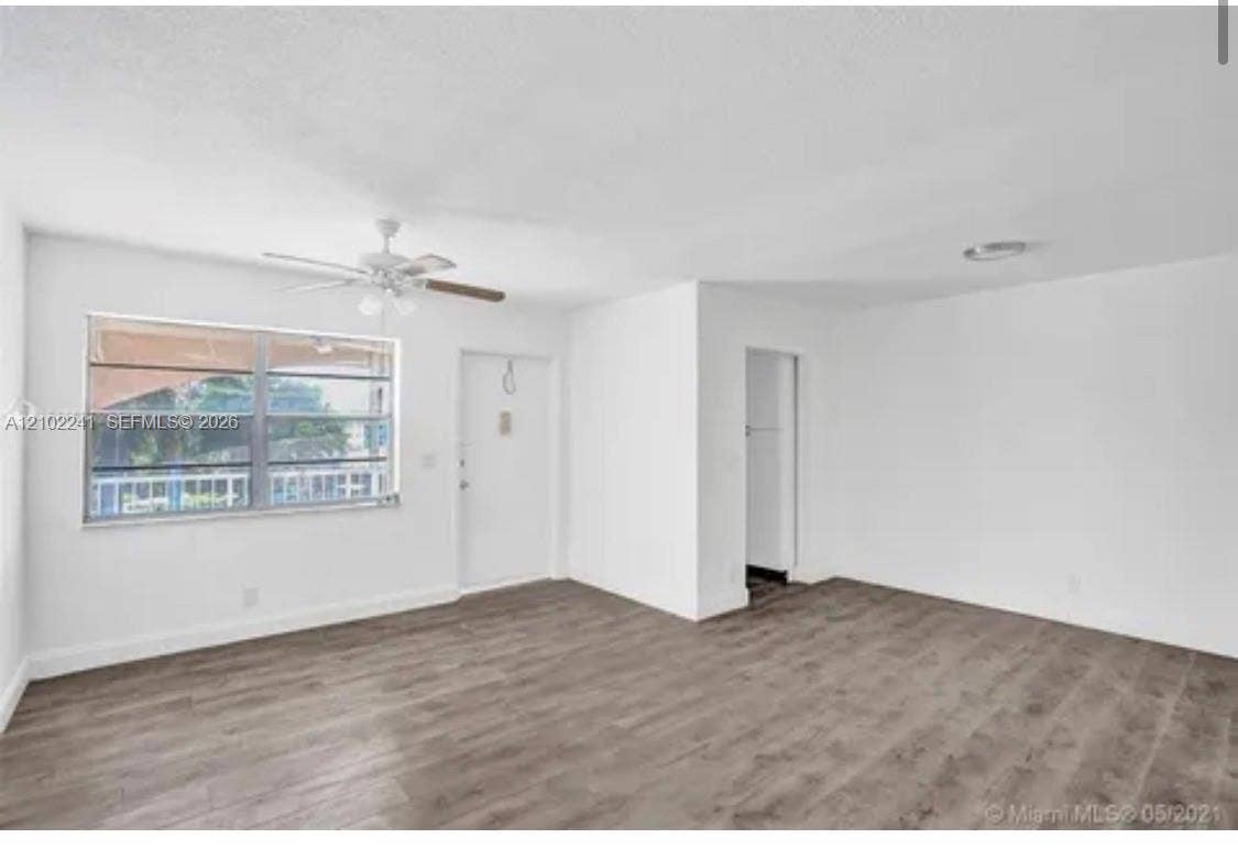 Neutral interior featuring wood-finish flooring, a multi-pane horizontal sliding window, a white single-panel entry door, and a ceiling-mounted fan with integrated light fixture