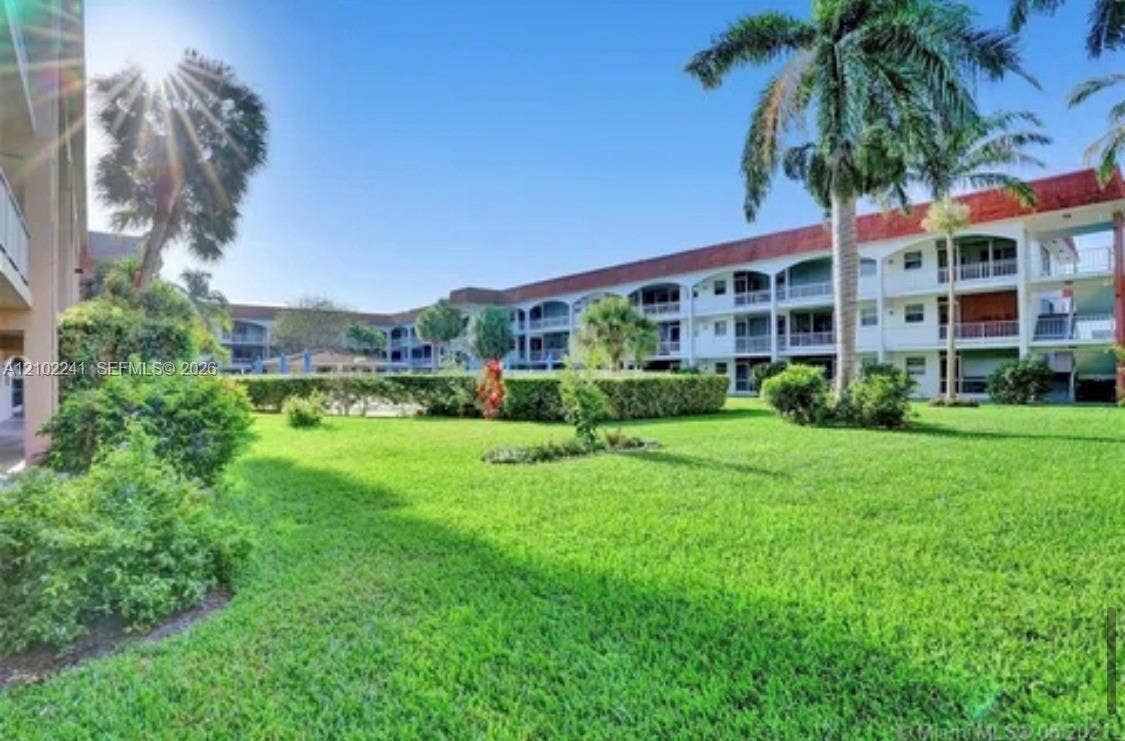 Multi-story residential structure featuring arched architectural detailing, expansive manicured lawn space, mature palm trees, and structured landscaping