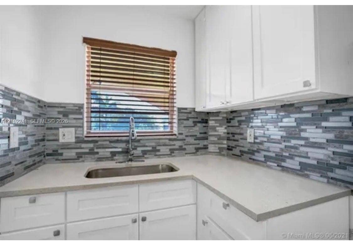 Kitchen featuring white shaker-style cabinetry, quartz countertops, a multi-tonal linear tile backsplash, and an undermount stainless steel sink with a high-arc faucet