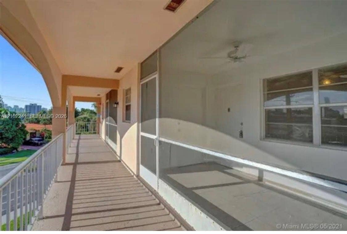 Covered exterior balcony featuring a metal railing, screened-in enclosure, and ceiling fan