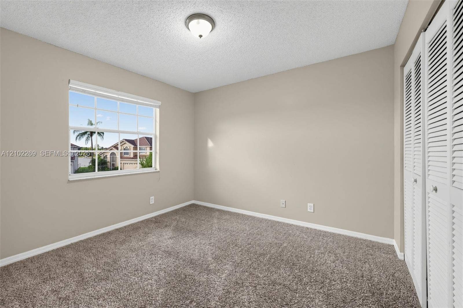 Room featuring neutral wall tones, wall-to-wall carpeting, a multi-pane window, and louvered bi-fold closet doors