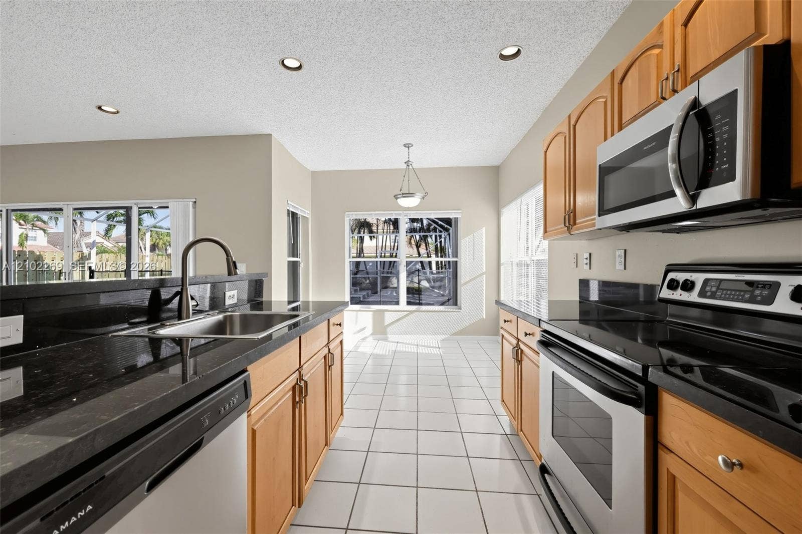 Kitchen featuring natural wood cabinetry, polished dark countertops, stainless steel appliances, ceramic tile flooring, and recessed ceiling lighting