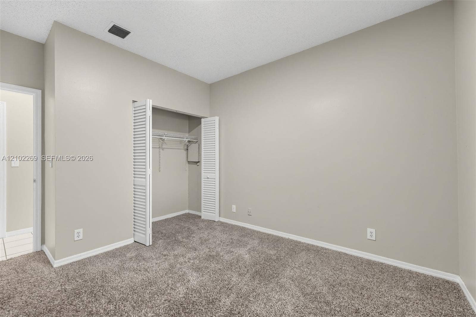Neutral-toned interior space featuring neutral carpeting, a built-in closet with bi-fold louvered doors, and wire shelving