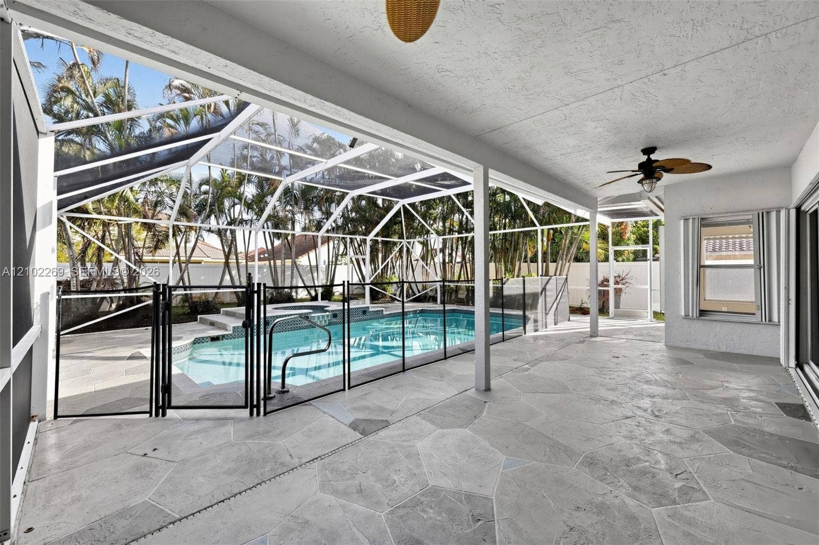Covered lanai featuring flagstone flooring and a ceiling fan, opening to a screened-in pool area with an attached spa and perimeter safety fencing