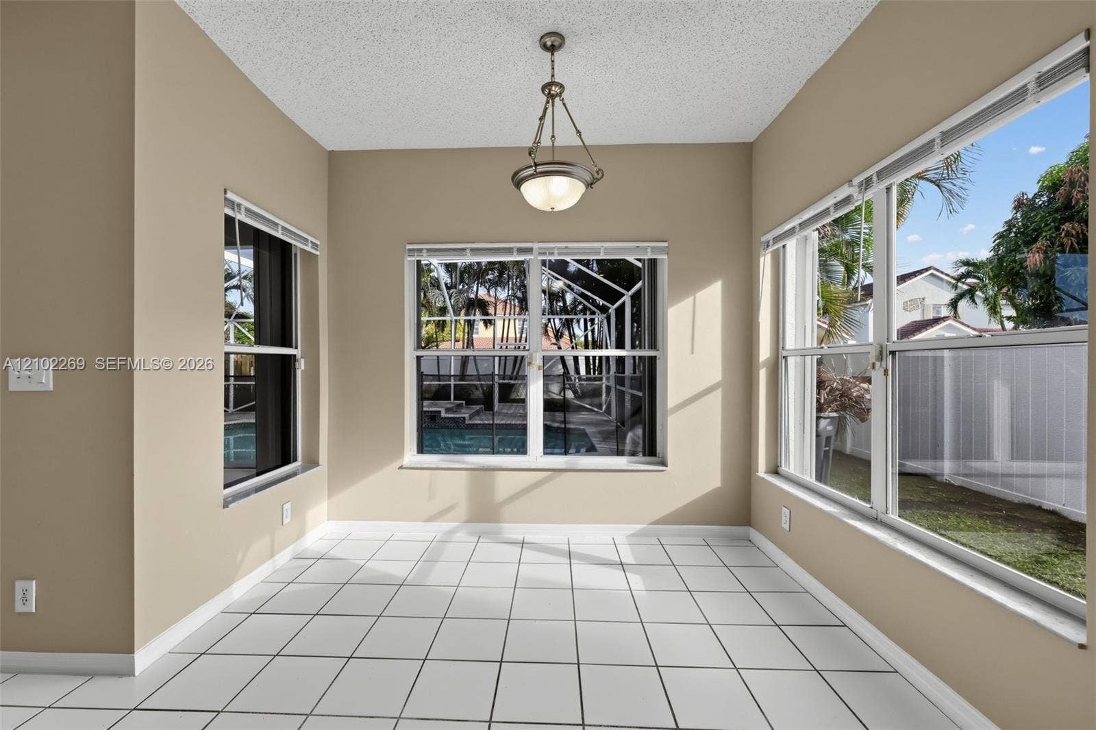 Sun-drenched room featuring large multi-pane windows, neutral tile flooring, and a central pendant light fixture