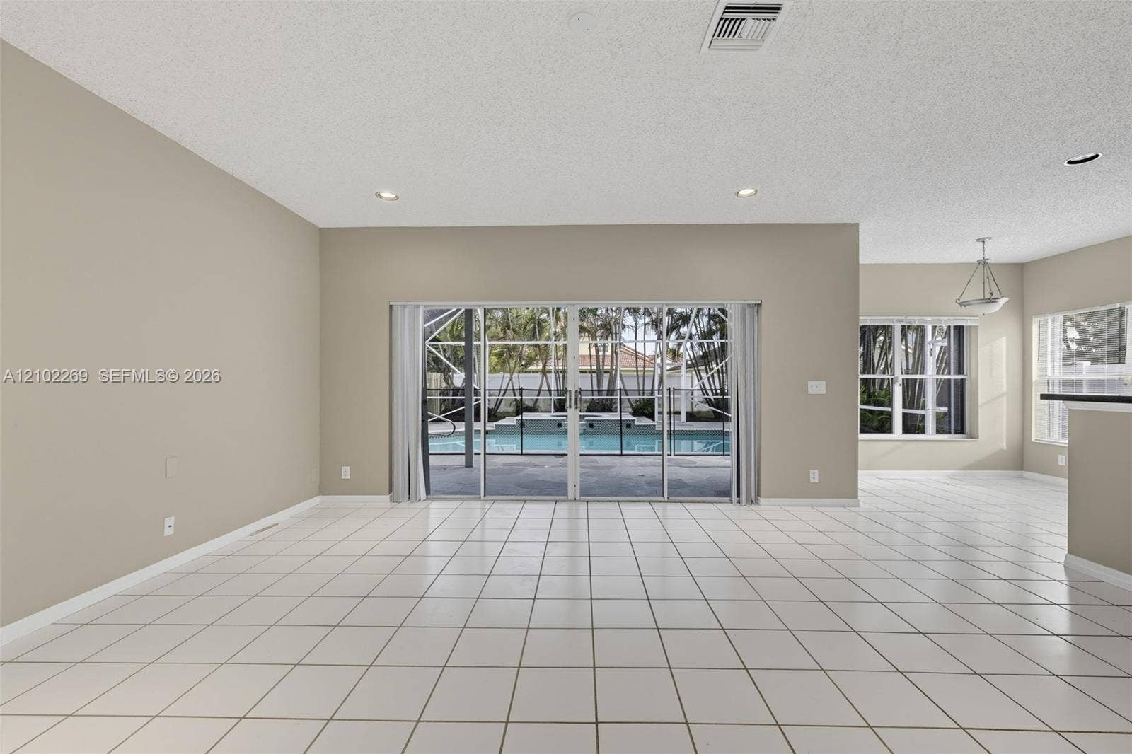 Open-concept space featuring large-format ceramic tile flooring, recessed lighting, and expansive glass sliding doors providing visibility to a screened-in pool and spa area