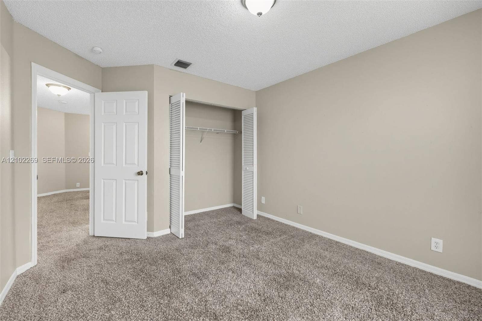 Neutral-toned interior featuring wall-to-wall carpeting, a reach-in closet with louvered bifold doors, and a paneled interior door