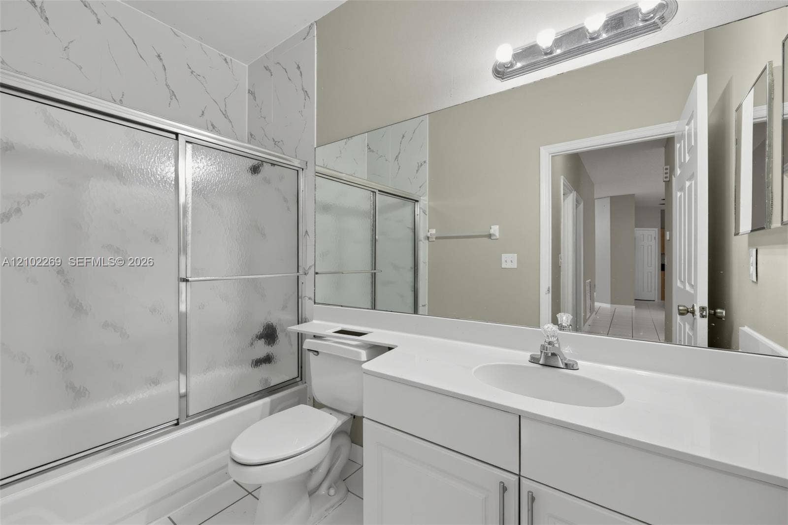 Bathroom featuring a white vanity with a solid surface countertop, an integrated oval sink, a full-width wall mirror, and a tub-shower combination with patterned wall surround and sliding glass doors