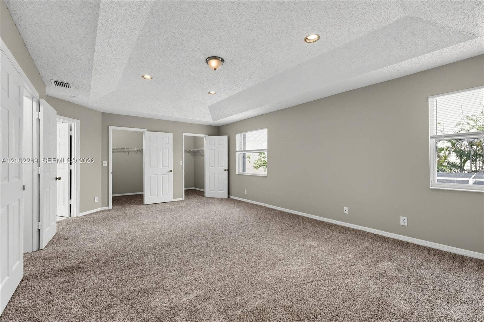Spacious interior featuring a tray ceiling, recessed lighting, wall-to-wall carpeting, and two built-in closet spaces with six-panel doors