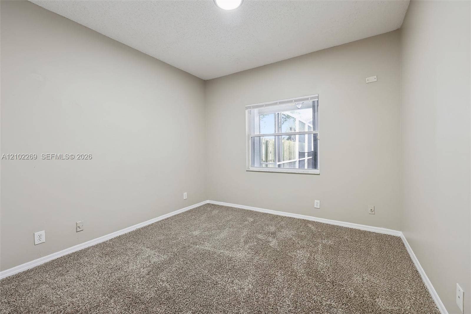 Neutral-toned interior space featuring neutral wall-to-wall carpeting, a single-pane window with white horizontal blinds, and overhead lighting