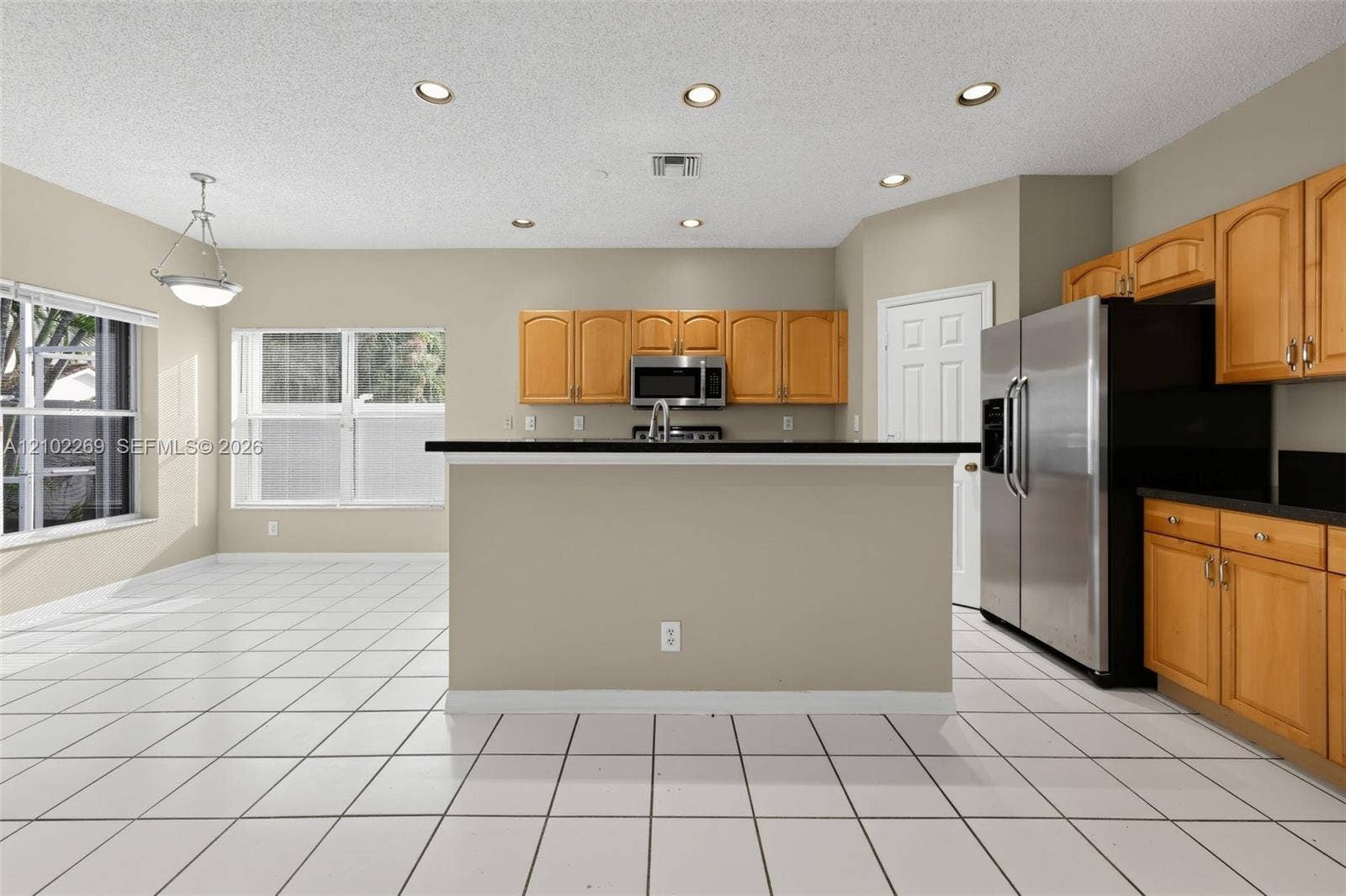 Kitchen featuring wood cabinetry, dark countertops, tile flooring, recessed lighting, and stainless steel refrigerator