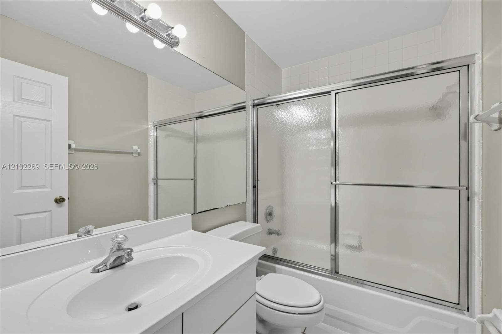 Bathroom featuring a white vanity with an integrated sink, a full-width vanity mirror, a multi-bulb light fixture, and a tub-shower combination with sliding glass doors