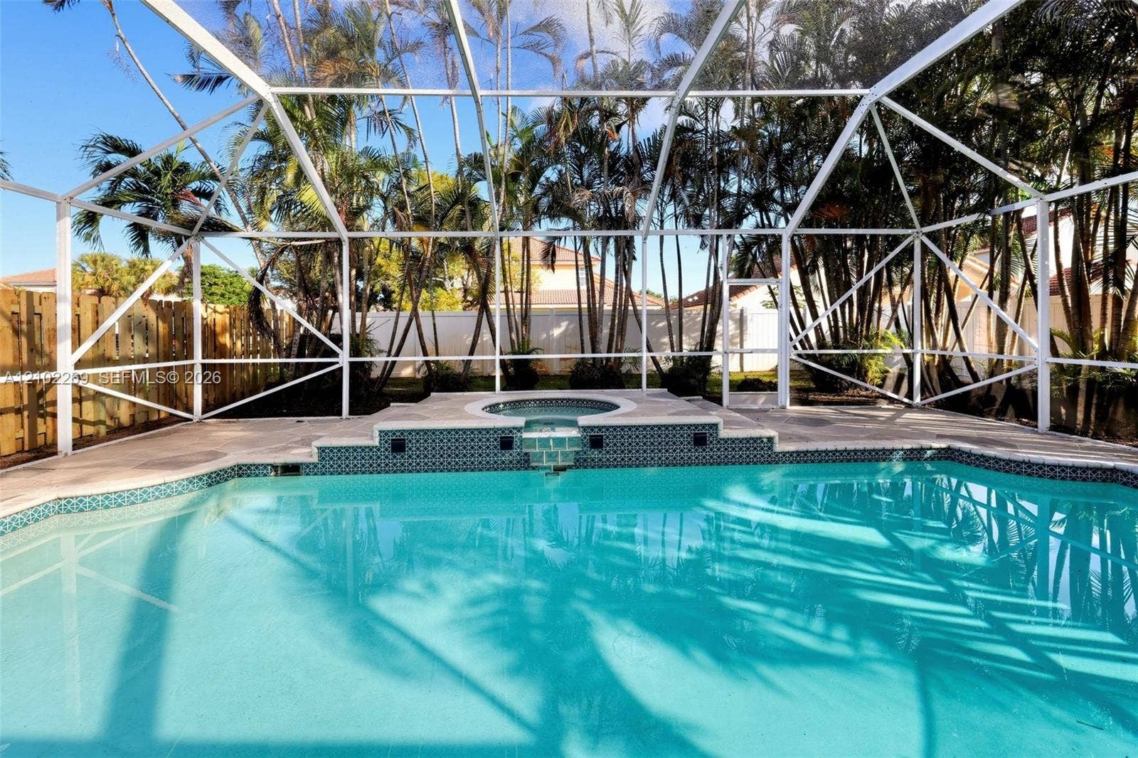 Screened lanai featuring a swimming pool, integrated spa, tiled water feature, and stone-finish decking