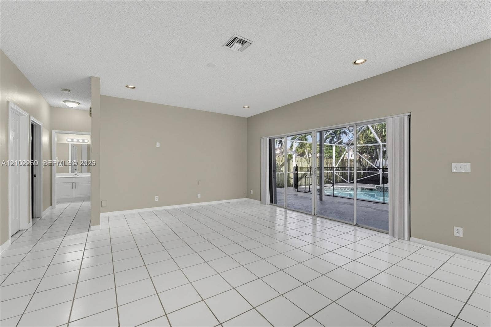 Open-concept interior featuring large-format tile flooring, recessed ceiling lighting, and expansive glass sliding doors providing visibility to a screened-in lanai with a pool