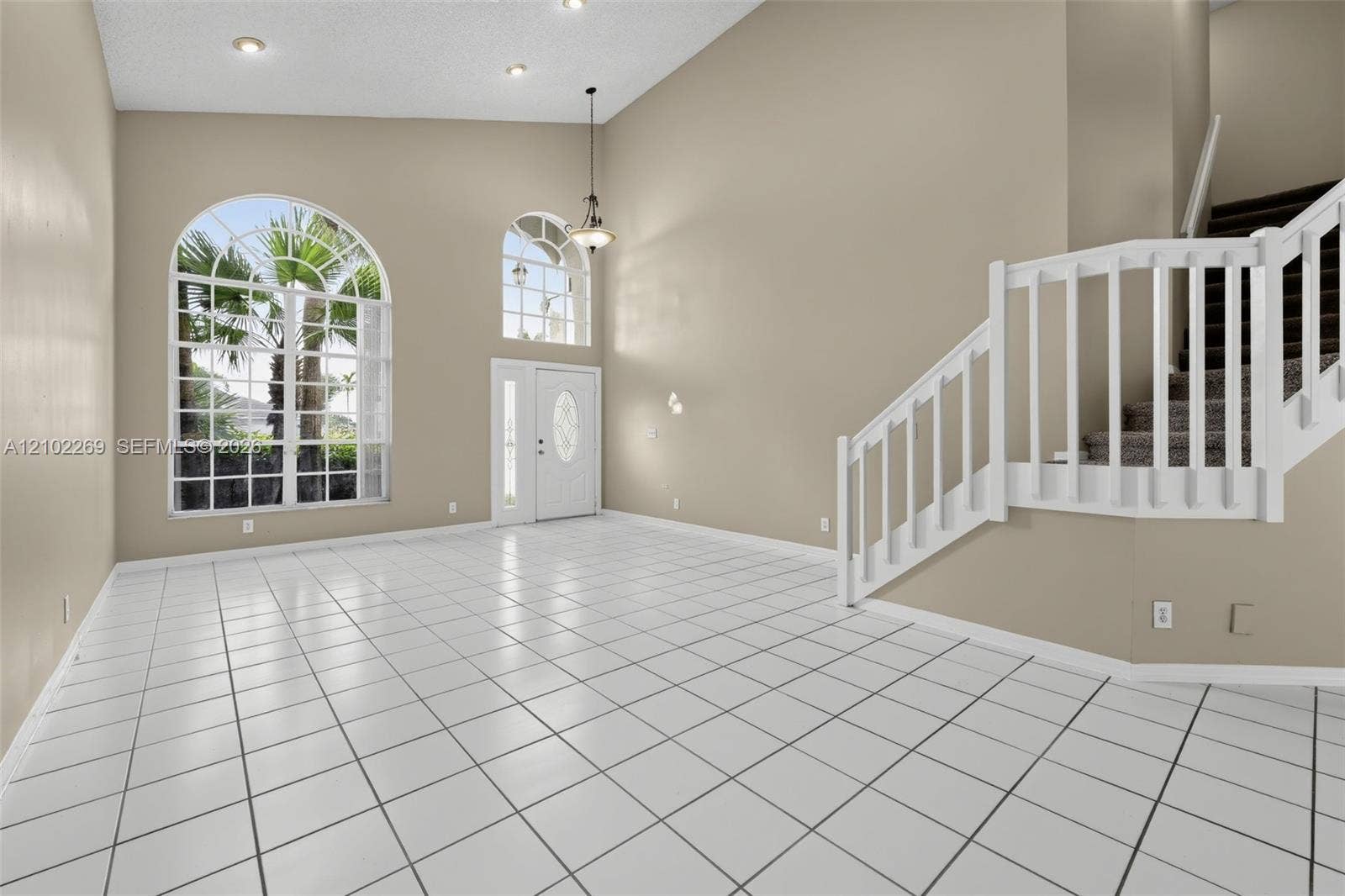 Vaulted ceiling with recessed lighting, large arched windows, tile flooring, and a white wooden staircase featuring a matching balustrade