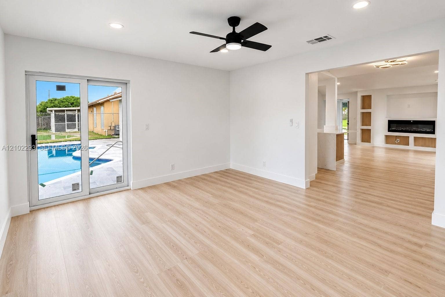 11056 NW 23rd Court, Sunrise, FL 33322 Open interior featuring light-tone wood-finish flooring, sliding glass doors, a contemporary black ceiling fan with integrated lighting, recessed lighting, and a built-in linear electric fireplace
