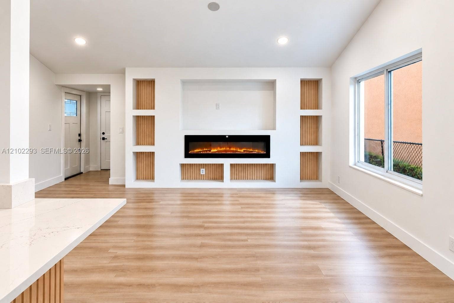 11056 NW 23rd Court, Sunrise, FL 33322 Custom built-in shelving featuring light wood-finish slat accents, integrated electric fireplace, recessed ceiling lighting, and wood-finish flooring
