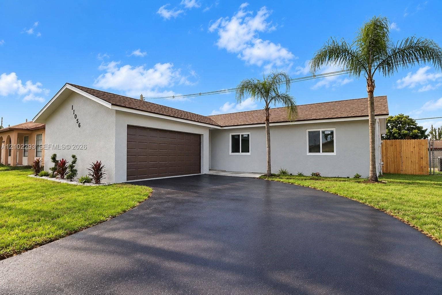 11056 NW 23rd Court, Sunrise, FL 33322 Single-story exterior featuring a stucco facade, an attached two-car garage, asphalt driveway, asphalt shingle roof, and established palm trees