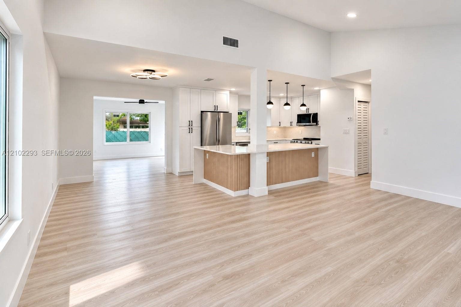 11056 NW 23rd Court, Sunrise, FL 33322 Open-concept interior featuring vaulted ceilings, light wood-finish flooring, a kitchen island with stone countertops, white shaker-style cabinetry, and pendant lighting