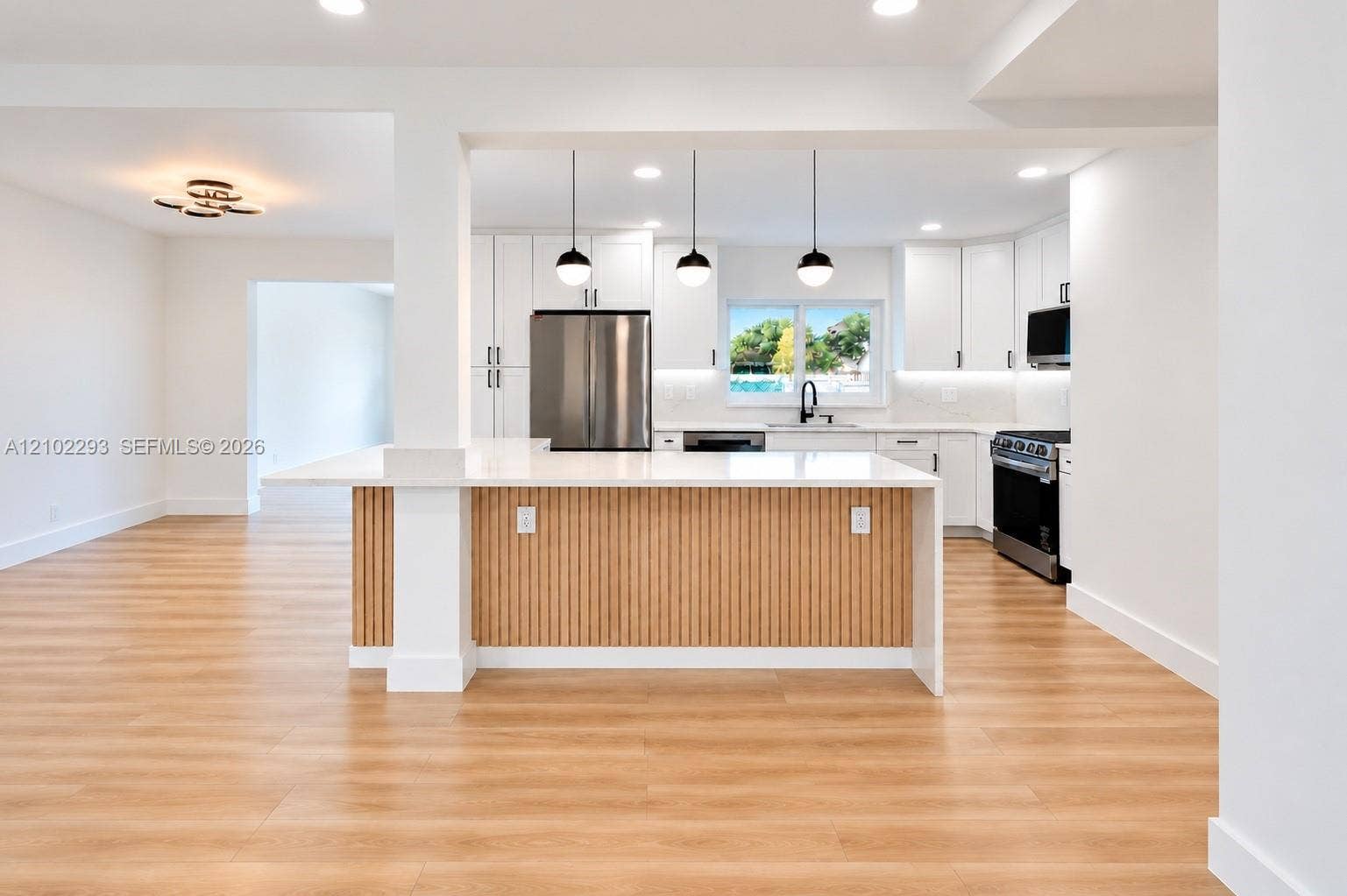 11056 NW 23rd Court, Sunrise, FL 33322 Kitchen featuring a tiered waterfall-edge island with slatted wood detailing, white shaker-style cabinetry, stainless steel appliances, recessed lighting, and wood-finish flooring