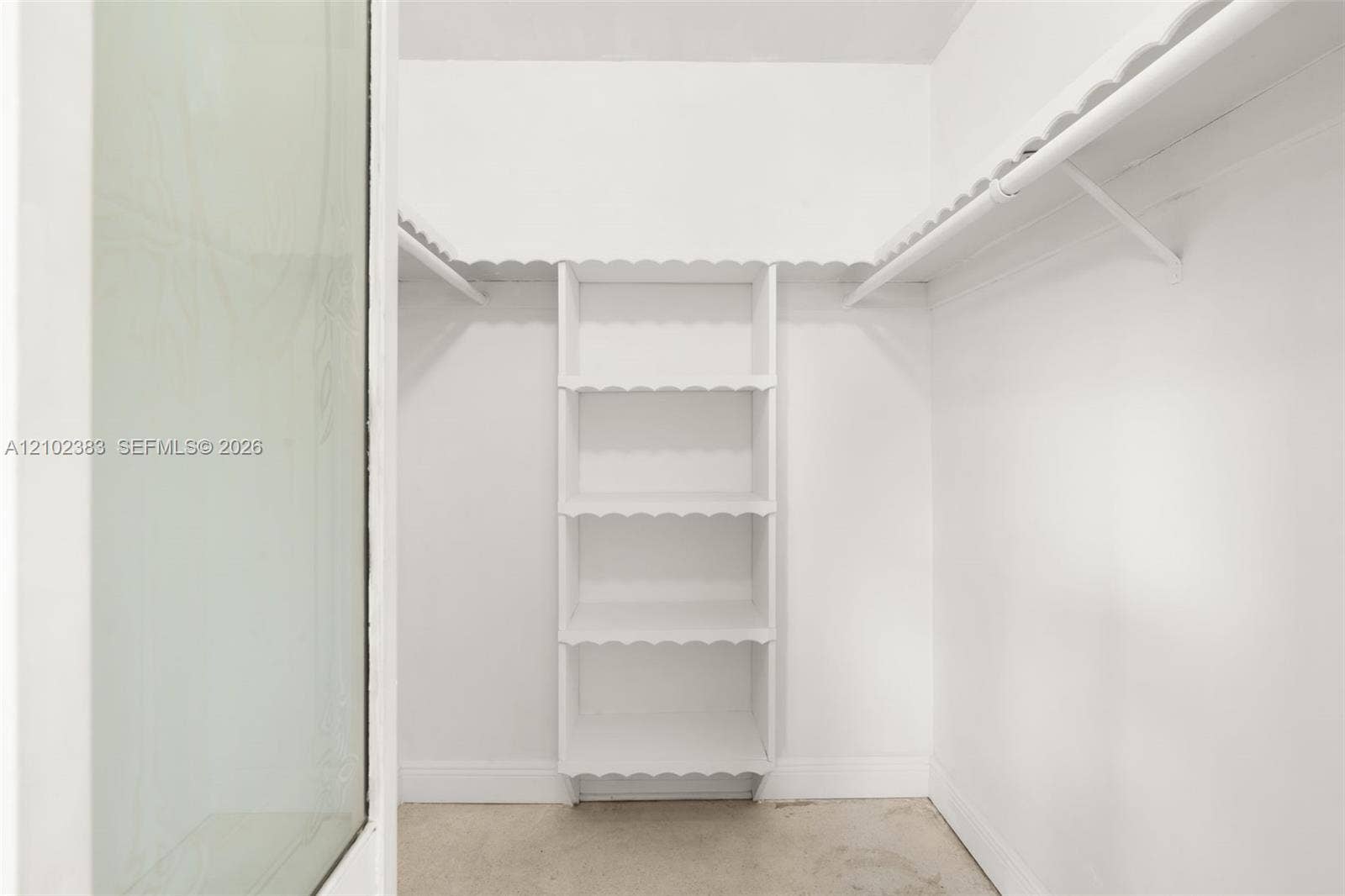 Primary walk-in closet featuring white built-in shelving, scalloped-edge wood trim, and a hanging rod