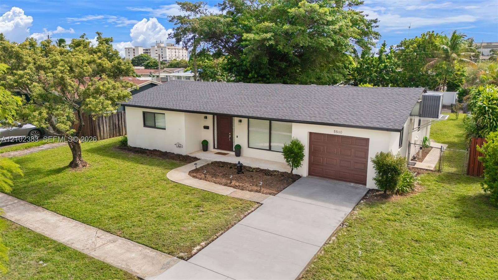 Single-story exterior featuring a light-toned stucco facade, shingled roof, concrete driveway, and covered front entry
