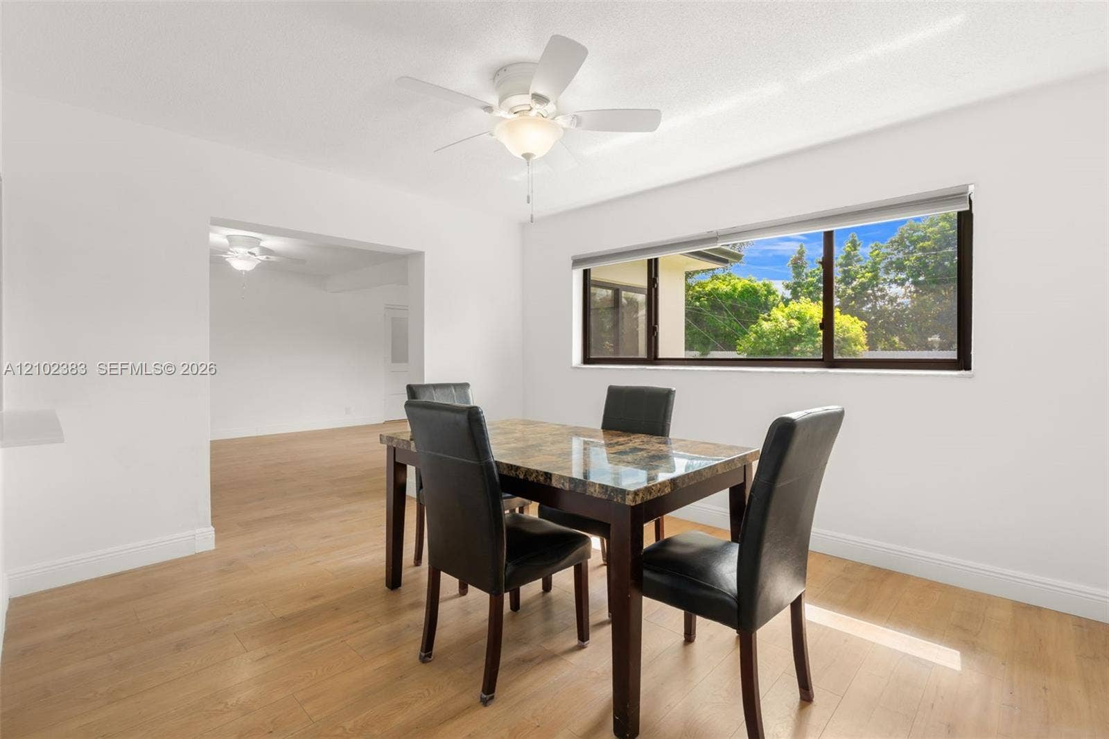 Breakfast area featuring wood-finish flooring, a neutral color palette, a wide-panel window, and a ceiling-mounted light fixture with a fan