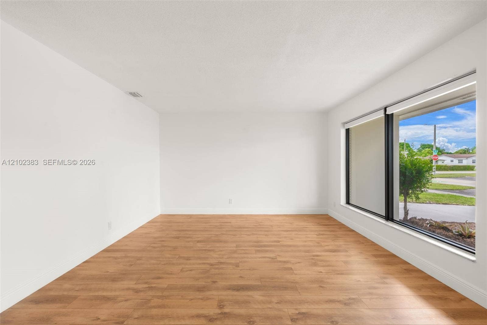 Neutral-toned interior space featuring wood-finish flooring, a expansive picture window with black frames, and recessed lighting