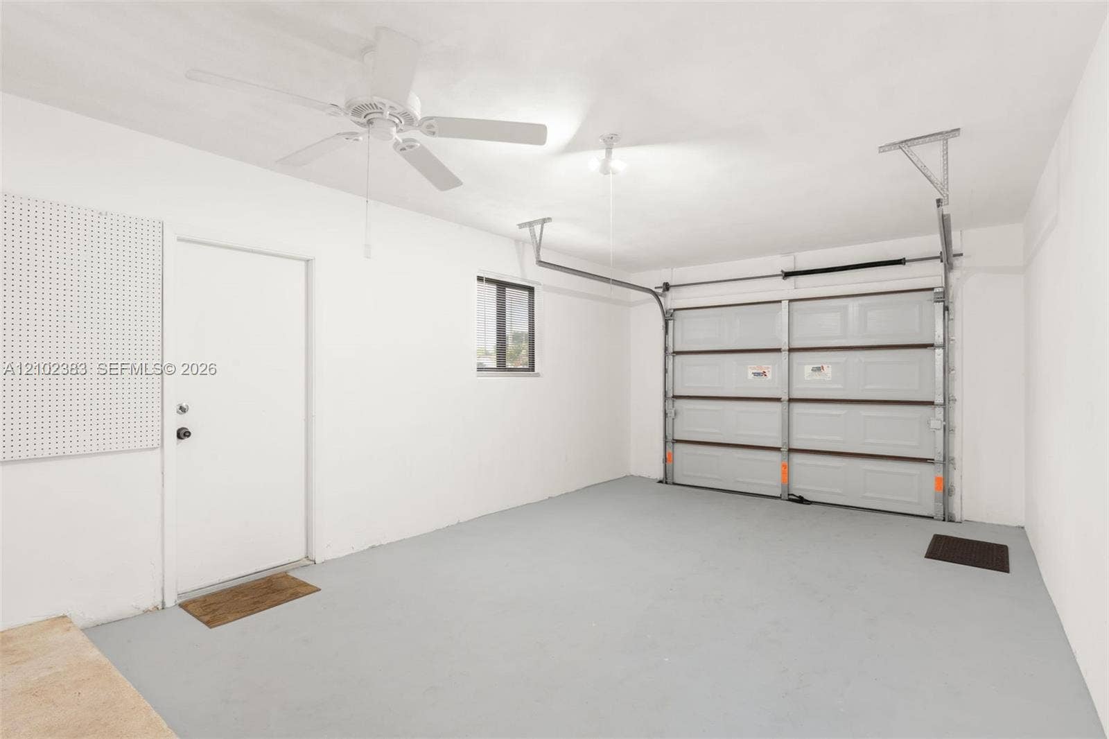 Enclosed garage featuring a multi-panel overhead door, finished concrete flooring, a ceiling-mounted fan, and integrated wall-mounted pegboard storage