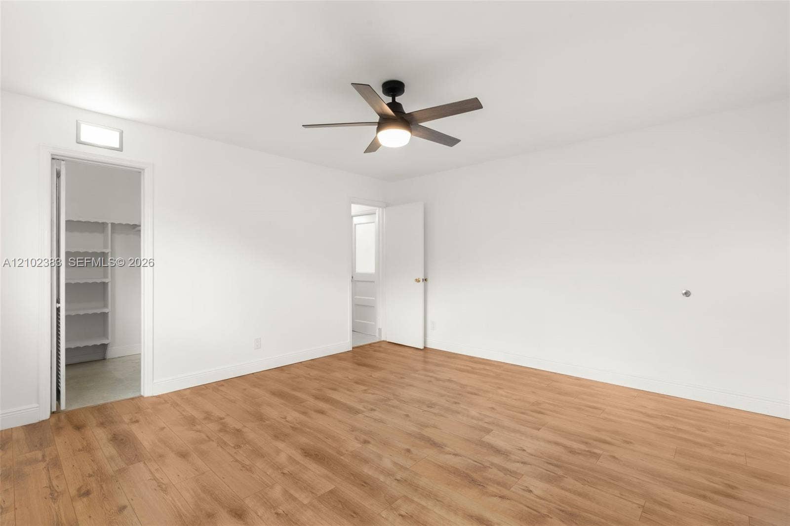 Primary bedroom Wood-finish flooring, multi-blade ceiling fan with integrated light, and walk-in closet with built-in shelving