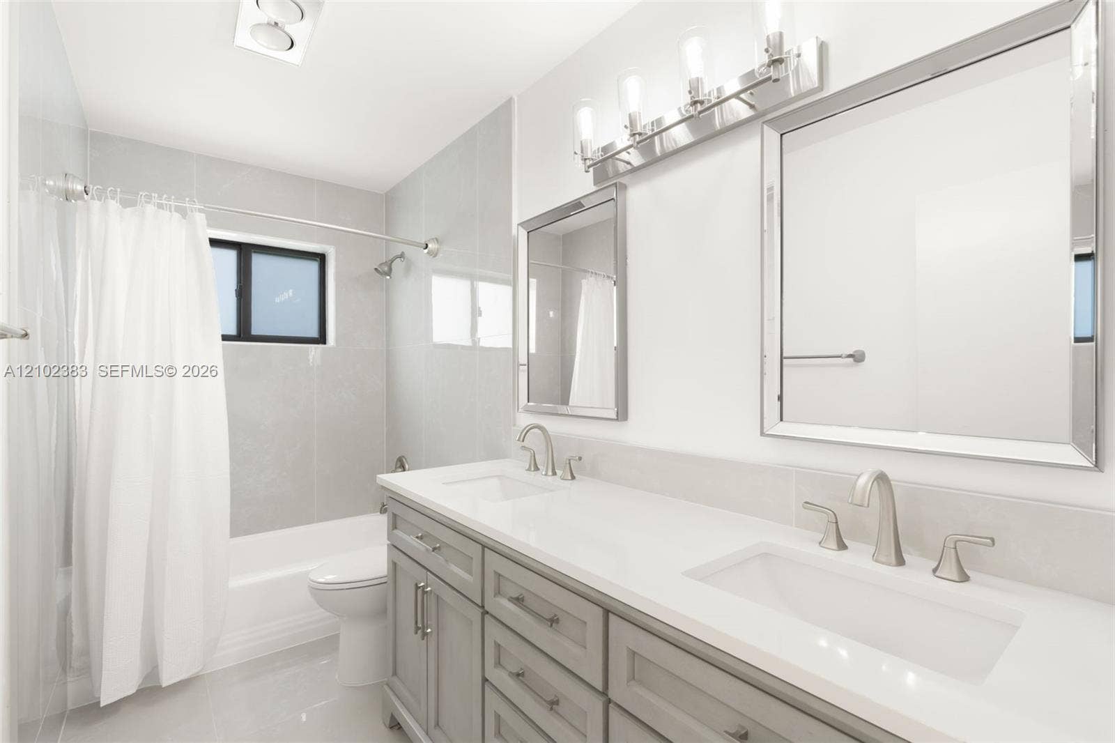 Bathroom featuring a dual-sink vanity with a solid-surface countertop, rectangular undermount basins, brushed nickel hardware, and two framed wall mirrors