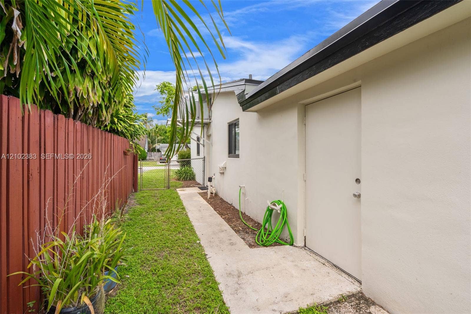 Exterior side walkway featuring a concrete path, stucco wall finish, metal fencing, and integrated outdoor lighting fixture