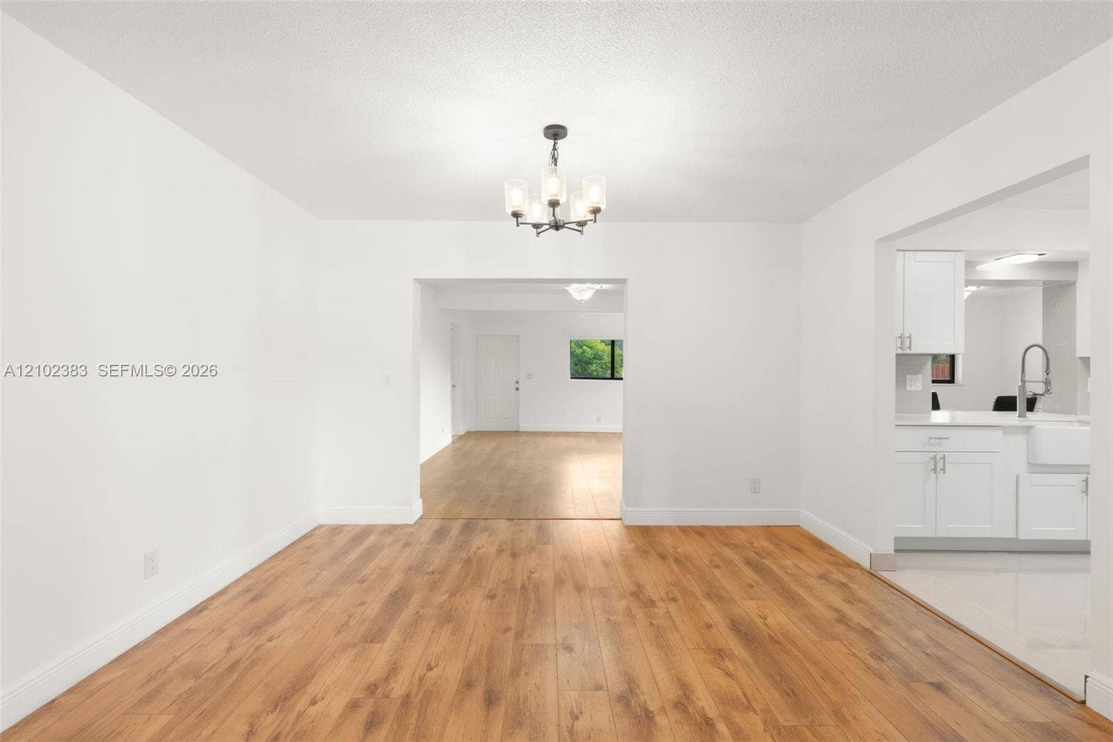 Dining area featuring wood-finish flooring, a contemporary multi-light chandelier, and white cabinetry with a farmhouse-style sink