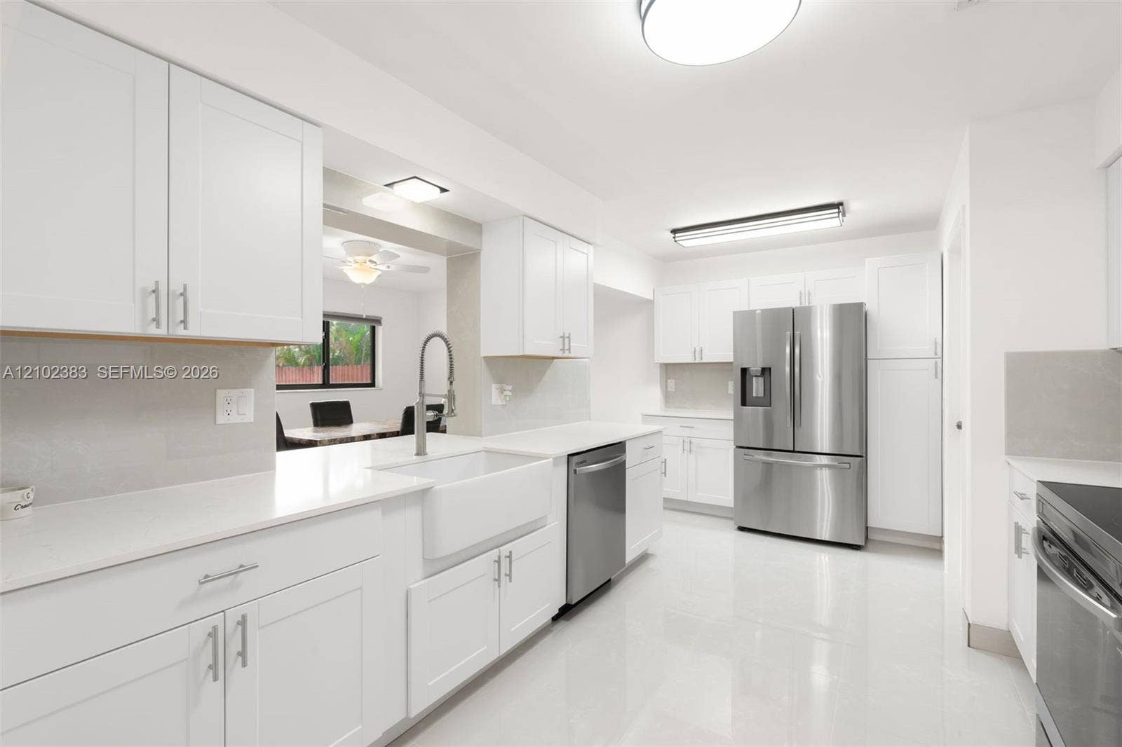Kitchen featuring white cabinetry, quartz countertops, a farmhouse-style apron sink, stainless steel appliances, and tile flooring
