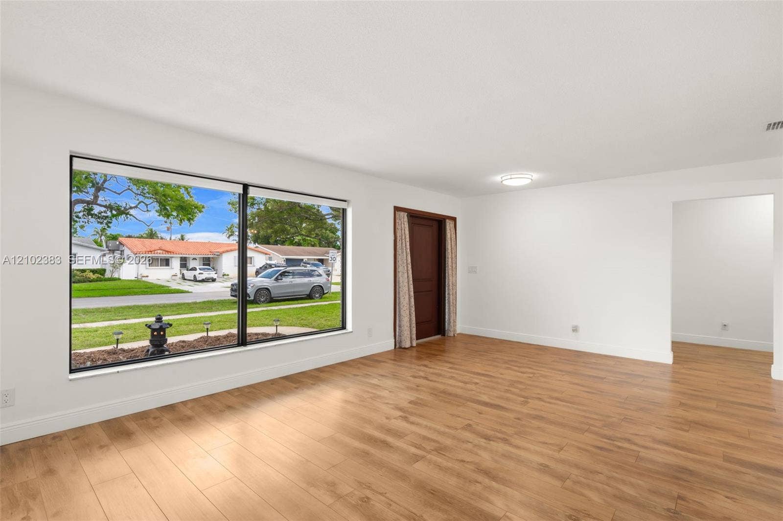 Interior space featuring wood-finish flooring, a large picture window, a solid-panel door, and a ceiling-mounted light fixture