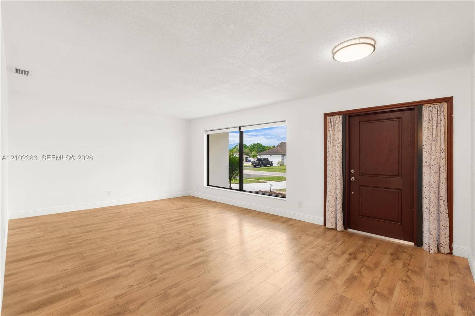 Interior space featuring wood-finish flooring, a large picture window, a solid wood-panel entry door, and a flush-mount ceiling light fixture