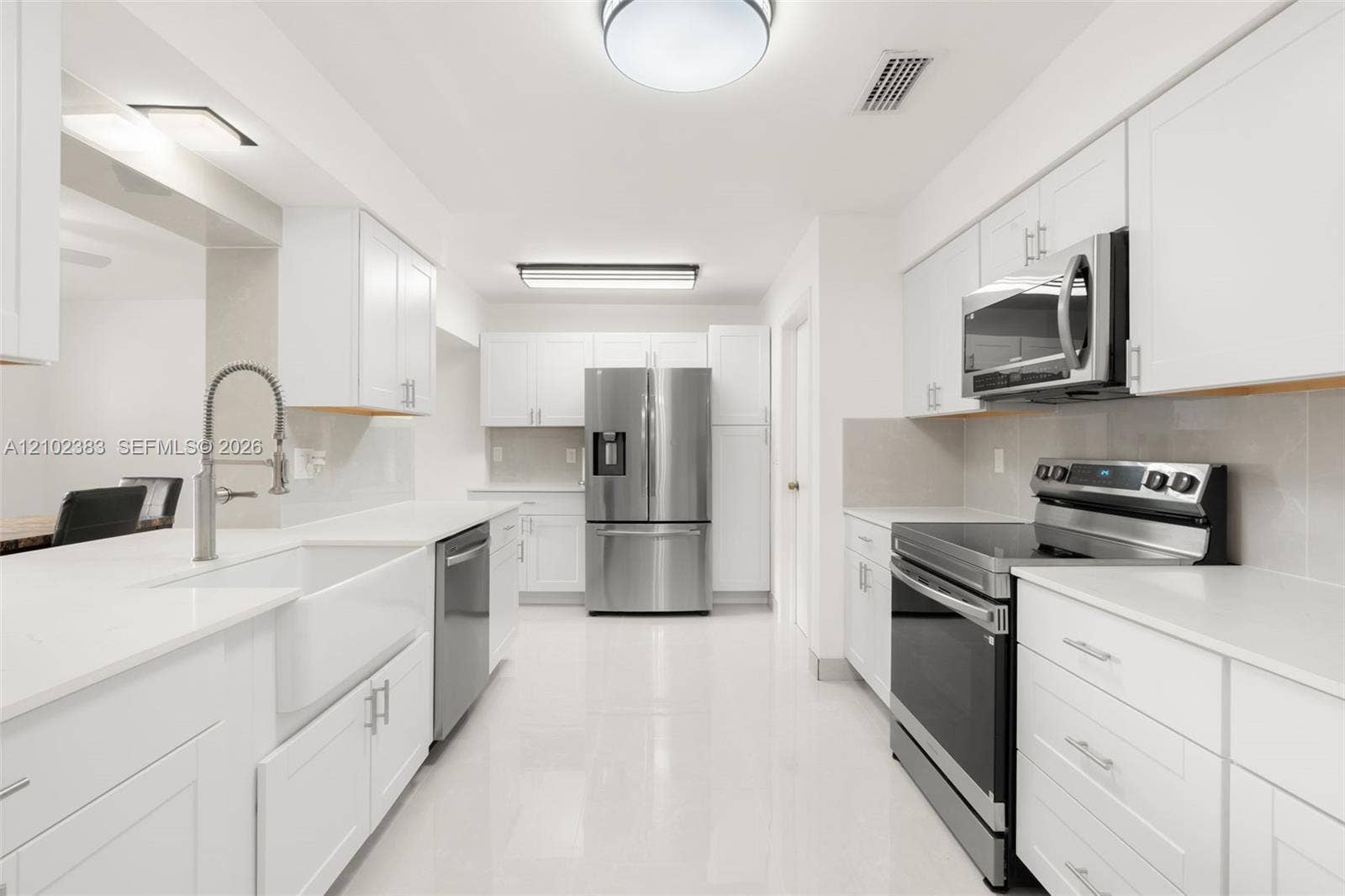 Kitchen featuring white cabinetry, solid-surface countertops, farmhouse sink with arched faucet, stainless steel appliances, and tile flooring