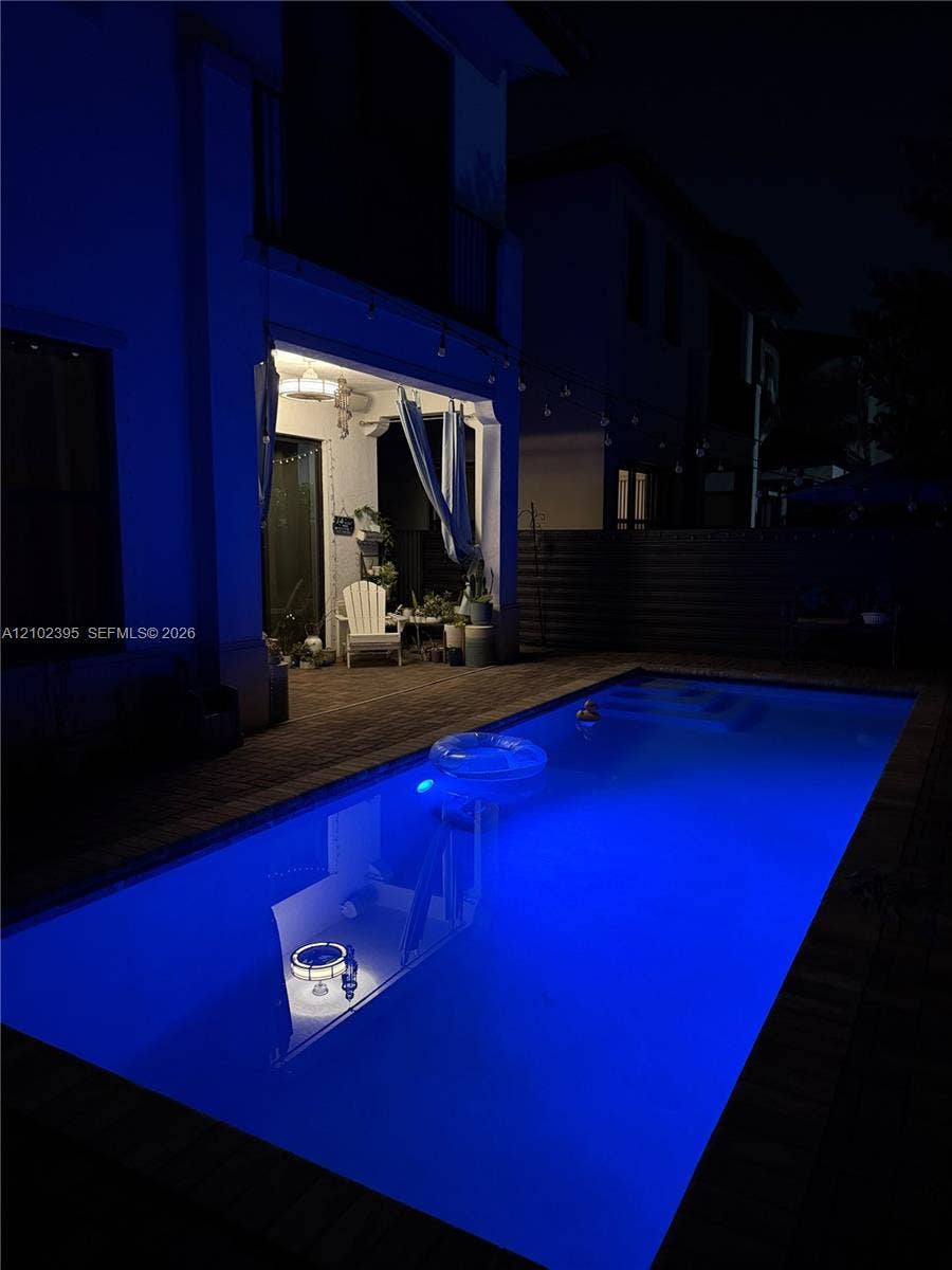 Rectangular in-ground swimming pool with brick paver decking and a covered patio featuring a built-in ceiling light fixture