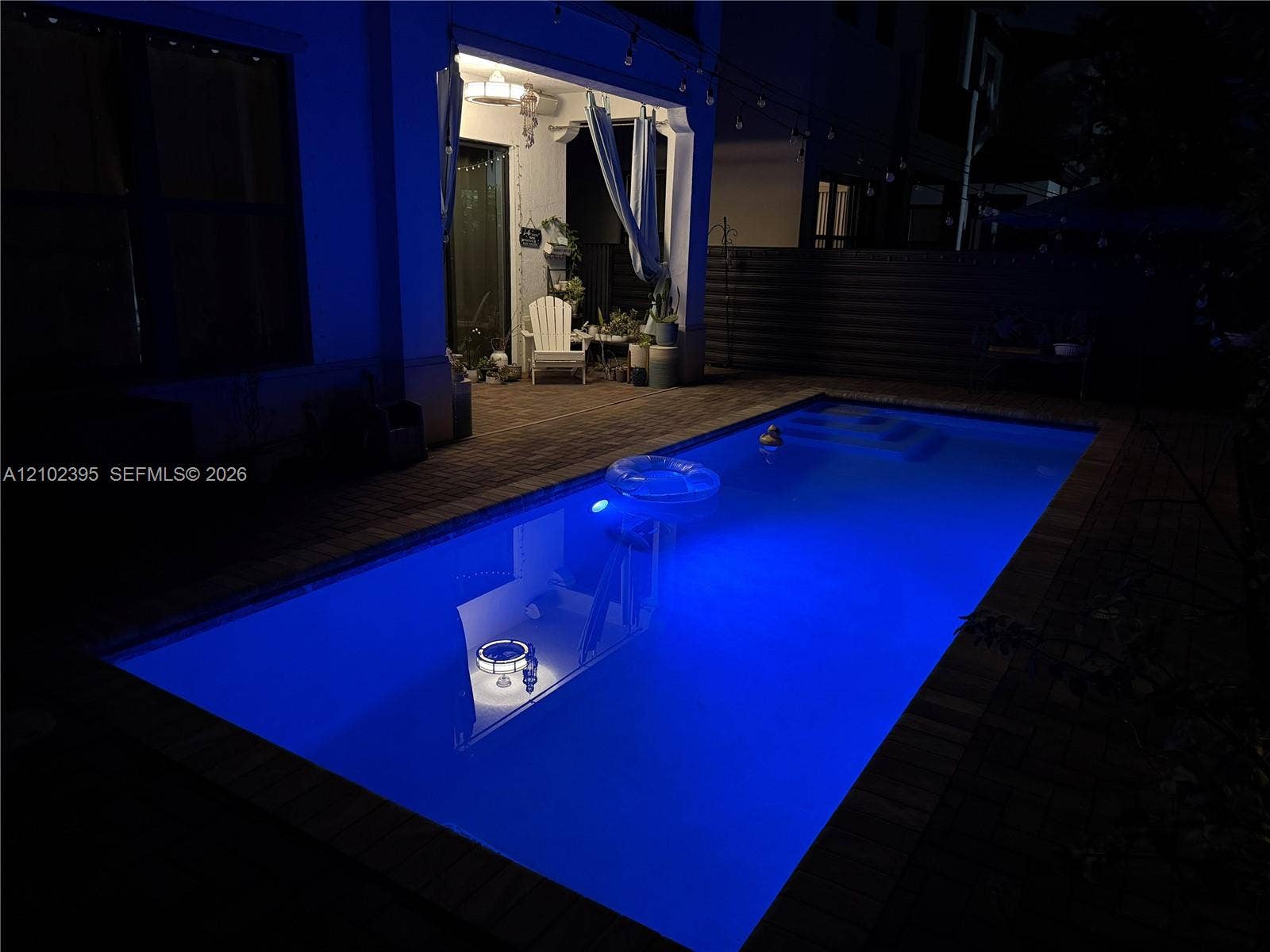 Rectangular inground pool with integrated lighting and stone-paver hardscaping, accompanied by a covered patio
