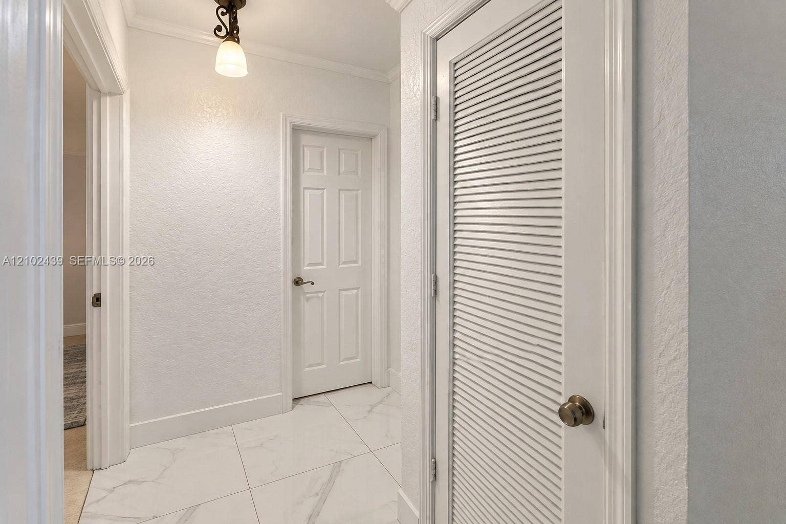 White tile flooring, crown molding, a built-in louvered door, a six-panel door, and a decorative ceiling light fixture