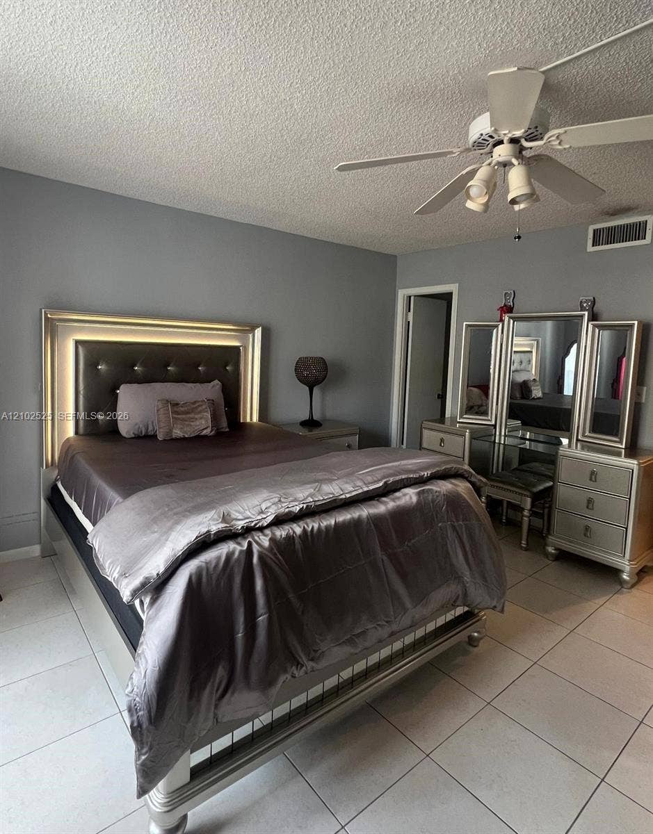 Neutral-toned interior space featuring light-colored ceramic tile flooring, solid grey wall finishes, and a ceiling-mounted light fixture with a multi-blade fan