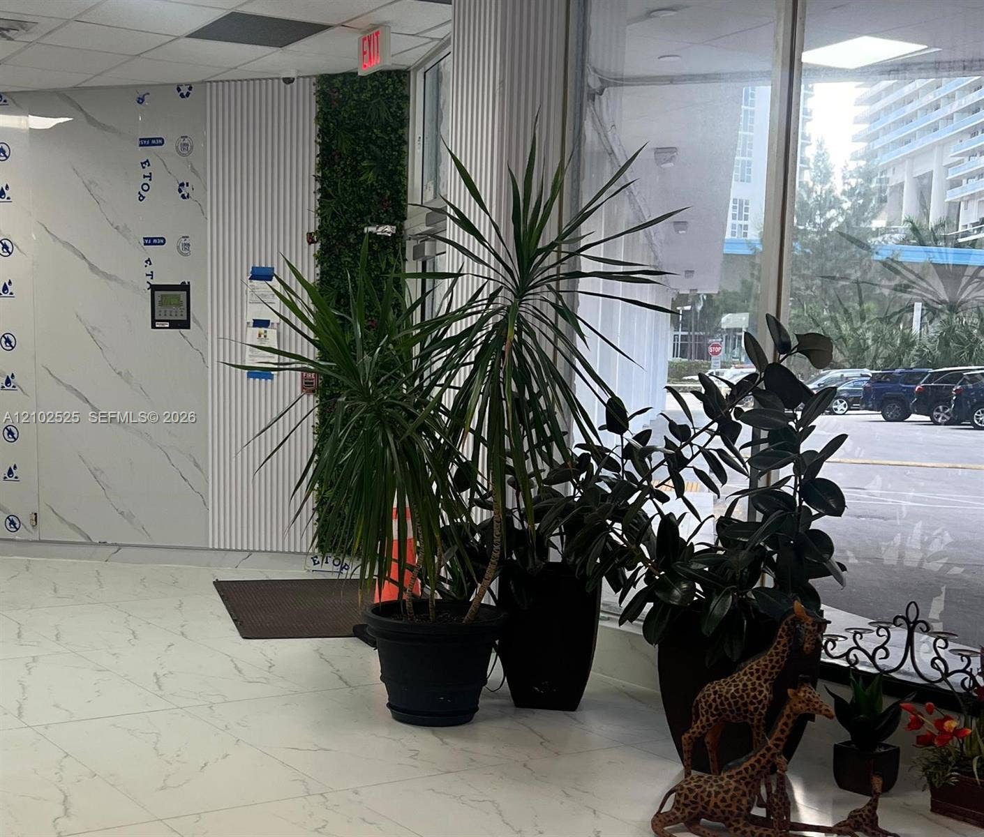 Large-format tile flooring with marble-pattern veining, floor-to-ceiling glass paneling, vertical fluted wall paneling, and an interior green wall feature