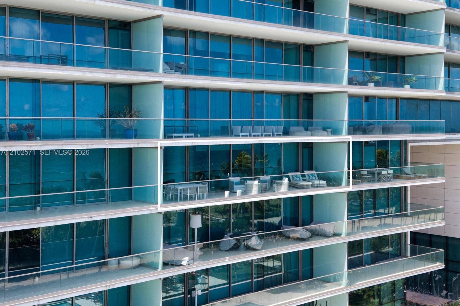 10201 Collins Avenue, #502, Bal Harbour, FL 33154 High-rise exterior featuring floor-to-ceiling blue-tinted glass windows and expansive private balconies with frameless glass railings