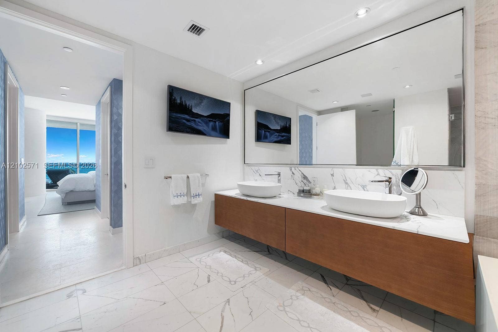 10201 Collins Avenue, #502, Bal Harbour, FL 33154 Floating wood-finish vanity with dual vessel sinks, stone-surface countertop, floor-to-ceiling mirror, and stone-finish tile flooring