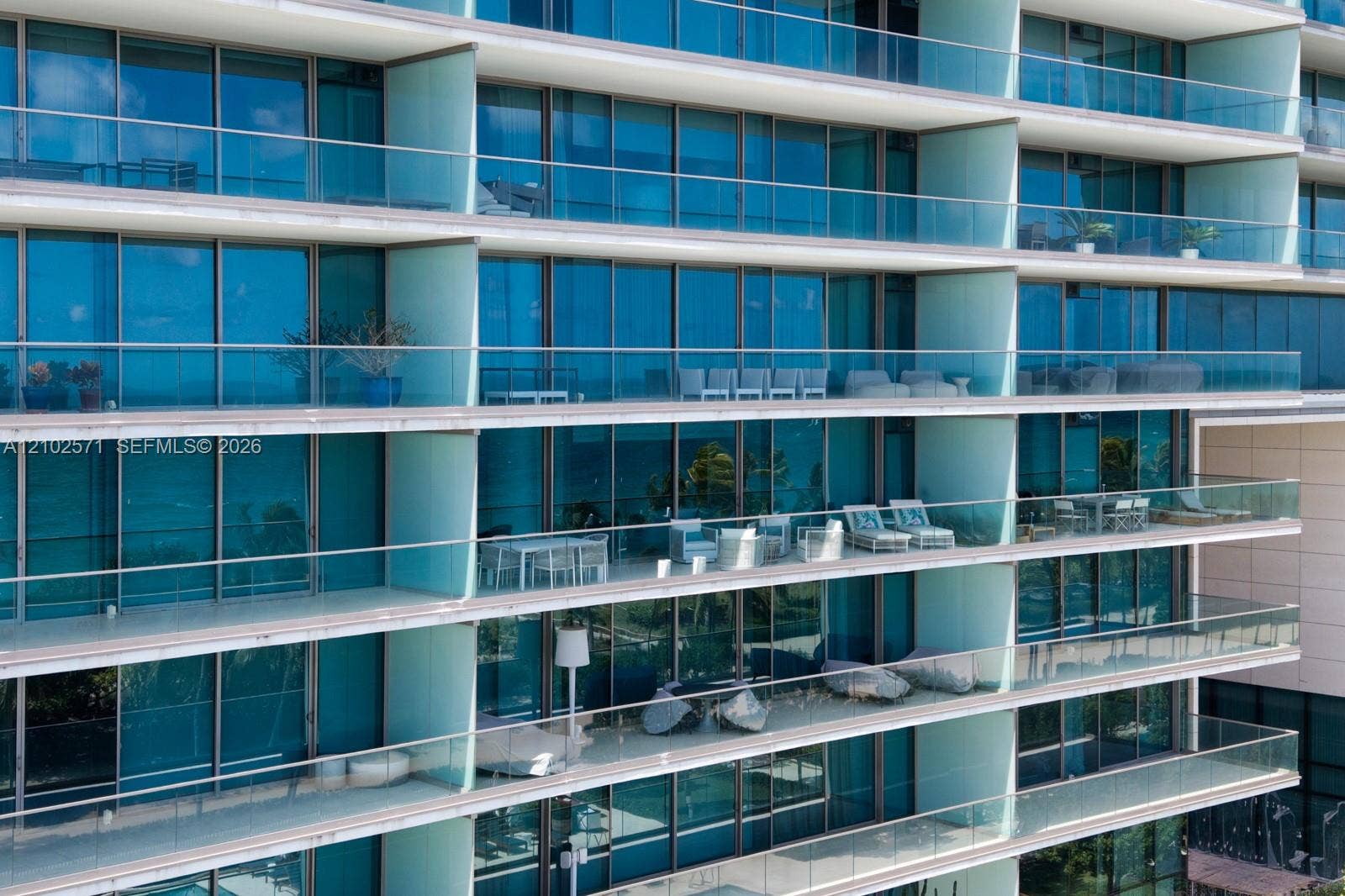 10201 Collins Avenue, #502, Bal Harbour, FL 33154 High-rise facade featuring floor-to-ceiling blue-tinted windows, full-width glass-railed balconies, and concrete slab terrace dividers