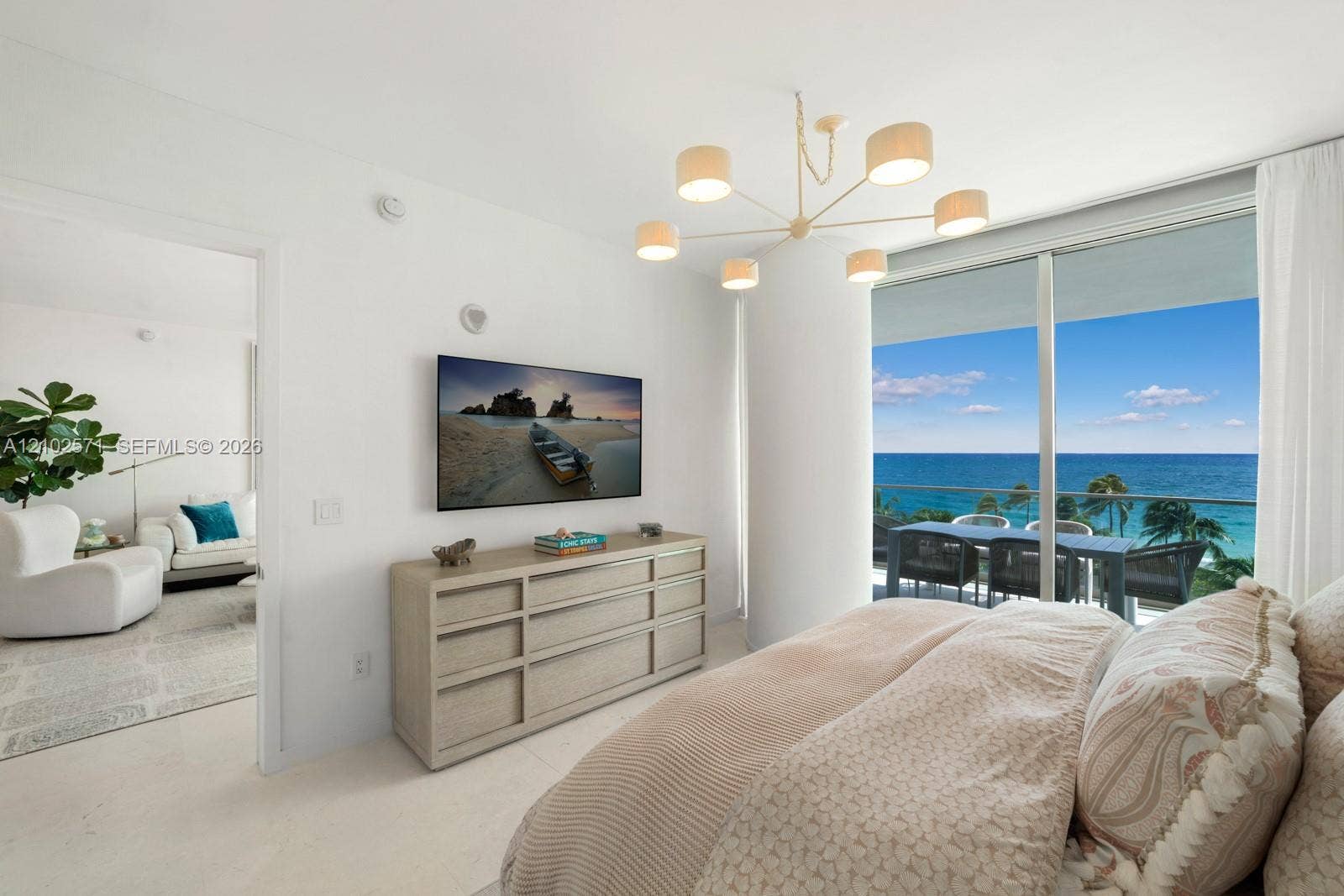 10201 Collins Avenue, #502, Bal Harbour, FL 33154 Full-height glass sliding doors, modern six-arm drum chandelier, and polished neutral-toned flooring with ocean backdrop and private balcony